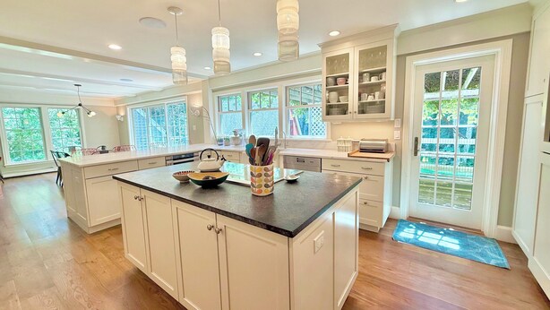A spacious kitchen with a large island, white cabinetry, and a view of the outdoors through large windows.