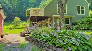 A green house with a covered porch, surrounded by a well-maintained garden with various plants and flowers.