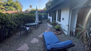 A patio area with a table and chairs, a blue lounge chair, and potted plants. - Charming guest cottage in Santa Barbara with access to hiking and the  beach (Santa Barbara)