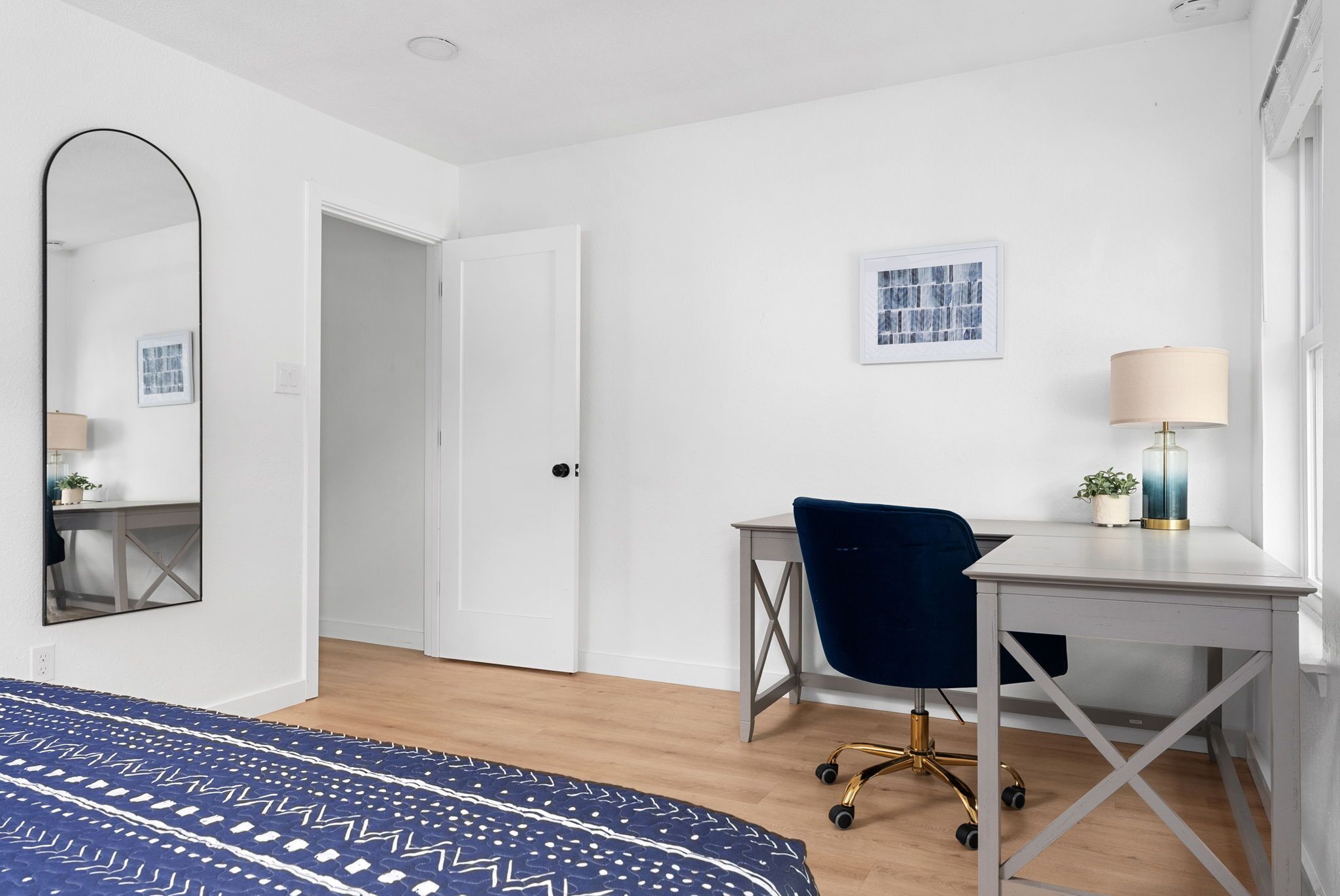 A bedroom with a bed, a desk, a chair, a lamp, and a mirror.