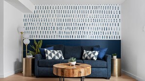 A modern living room with a blue sofa, a round wooden coffee table, and a decorative wall panel. - MCM Condo Near DT SoCo Pet Friendly (Austin)