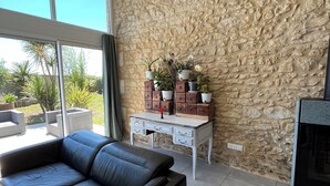 Una sala de estar moderna con una pared de piedra, un sofá de cuero negro, una mesa de centro blanca y un pequeño mueble blanco con plantas en macetas.