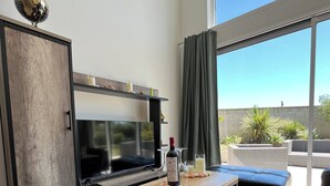 Una sala de estar moderna con televisor, un mueble de madera, una mesa con un tablero de ajedrez y un ventanal con vistas a zonas verdes.