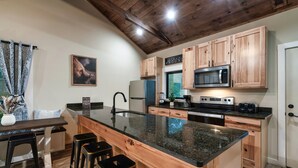 A kitchen with wooden cabinets, a granite countertop, a microwave, a stove, and a sink. - Modern Cabin Near Pigeon Forge, Sleeps 8, Hot Tub, Game Room & Fire Pit (Sevierville)