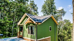 A small, green cabin with a sloped roof, a porch, and a stone foundation. - Modern Cabin Near Pigeon Forge, Sleeps 8, Hot Tub, Game Room & Fire Pit (Sevierville)