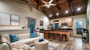 A spacious living room with a white sofa, a round coffee table, and a wooden ceiling. - Modern Cabin Near Pigeon Forge, Sleeps 8, Hot Tub, Game Room & Fire Pit (Sevierville)