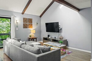 Una sala de estar moderna con un sofá gris, una mesa de centro, un televisor y una mesita auxiliar con una lámpara.