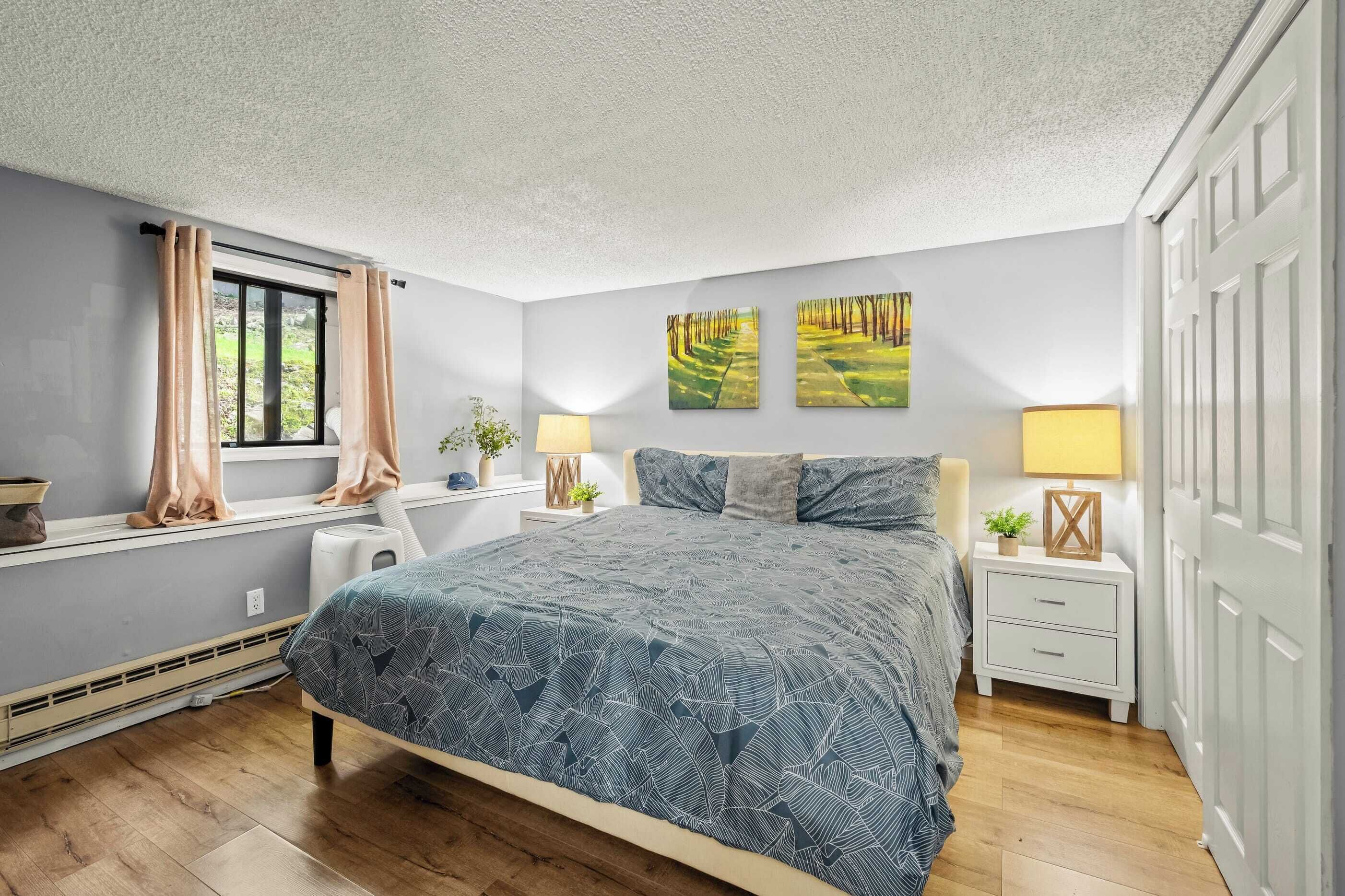 Une chambre à coucher comprenant un lit, des tables de chevet, une fenêtre avec des rideaux et deux tableaux accrochés au mur.