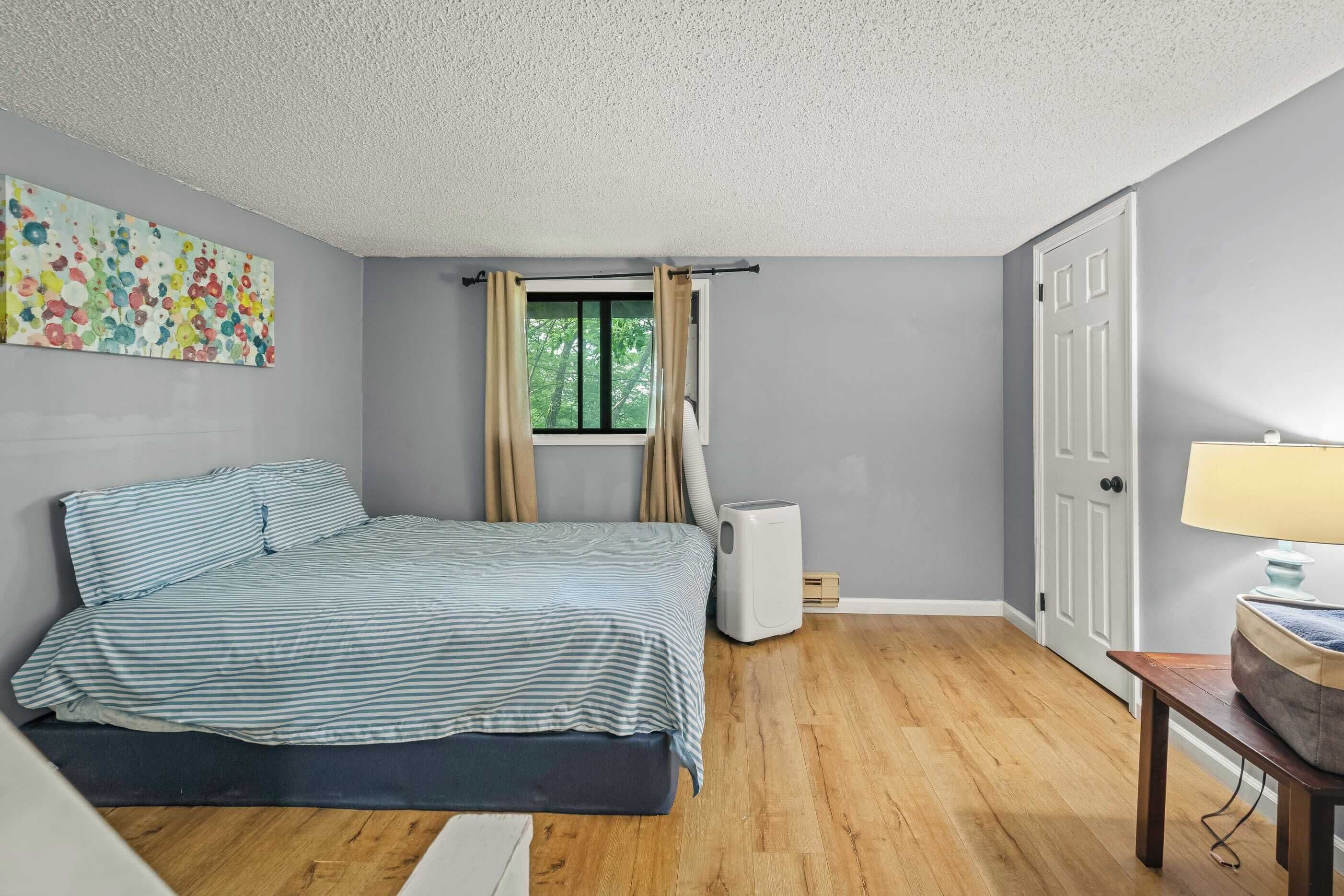 A bedroom with a bed, a window with curtains, a radiator, a door, and a lamp on a table.
