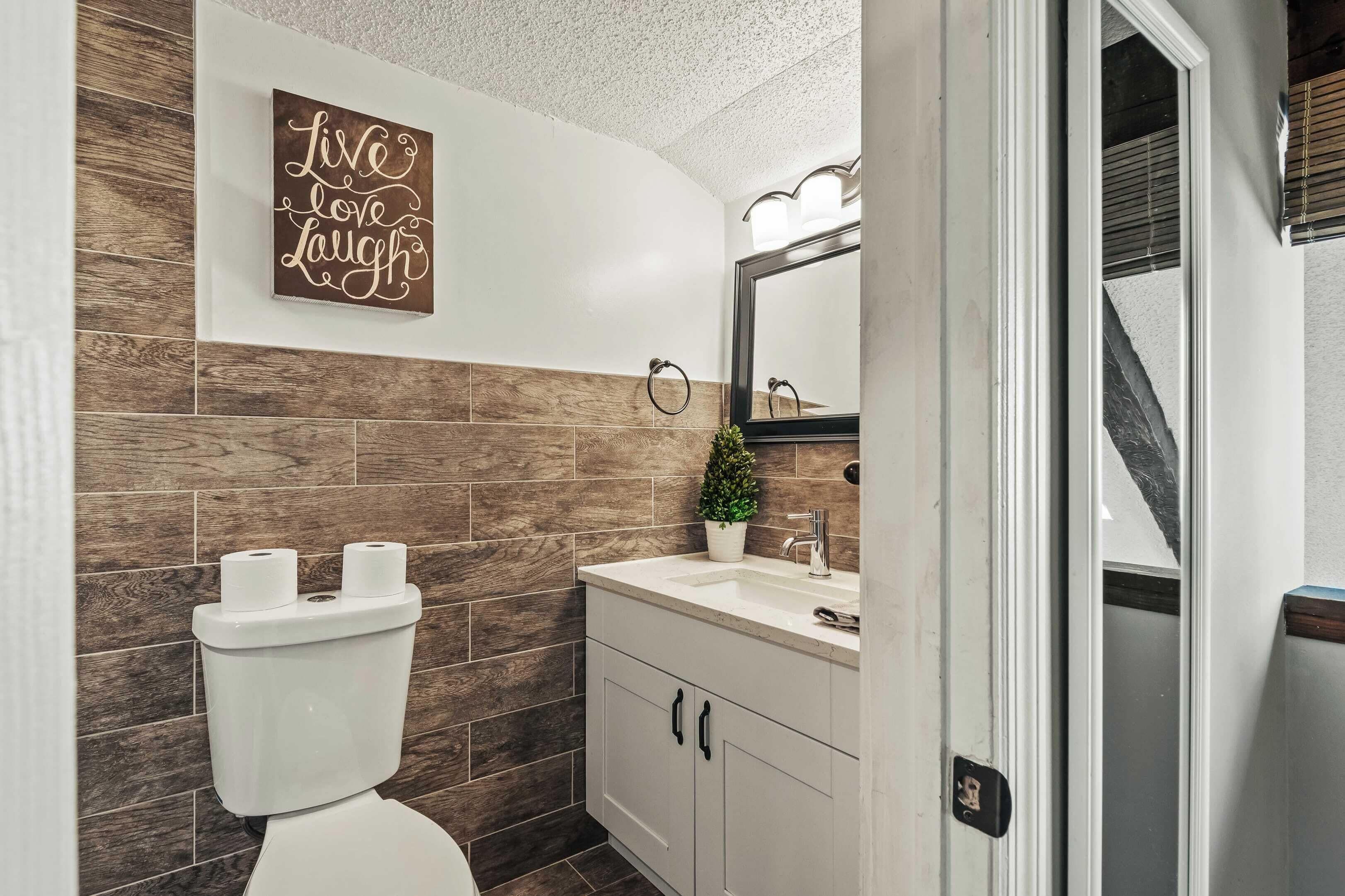 A modern bathroom with a wooden wall, a toilet, a sink with a mirror, and a decorative sign.