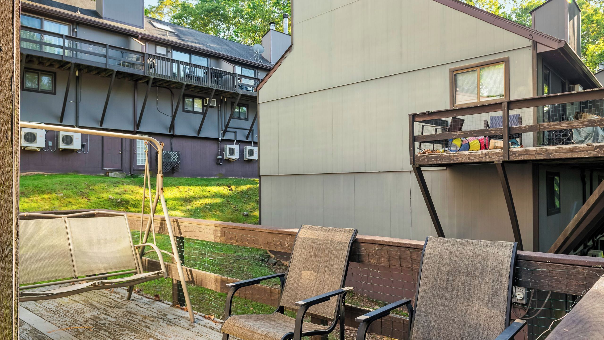 Una terraza con mobiliario exterior, vista a un edificio con múltiples ventanas y un balcón, y una zona con césped.