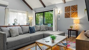 Ein modernes Wohnzimmer mit einem grauen Ecksofa, einem Couchtisch mit Pflanze und einem farbenfrohen Teppich.
