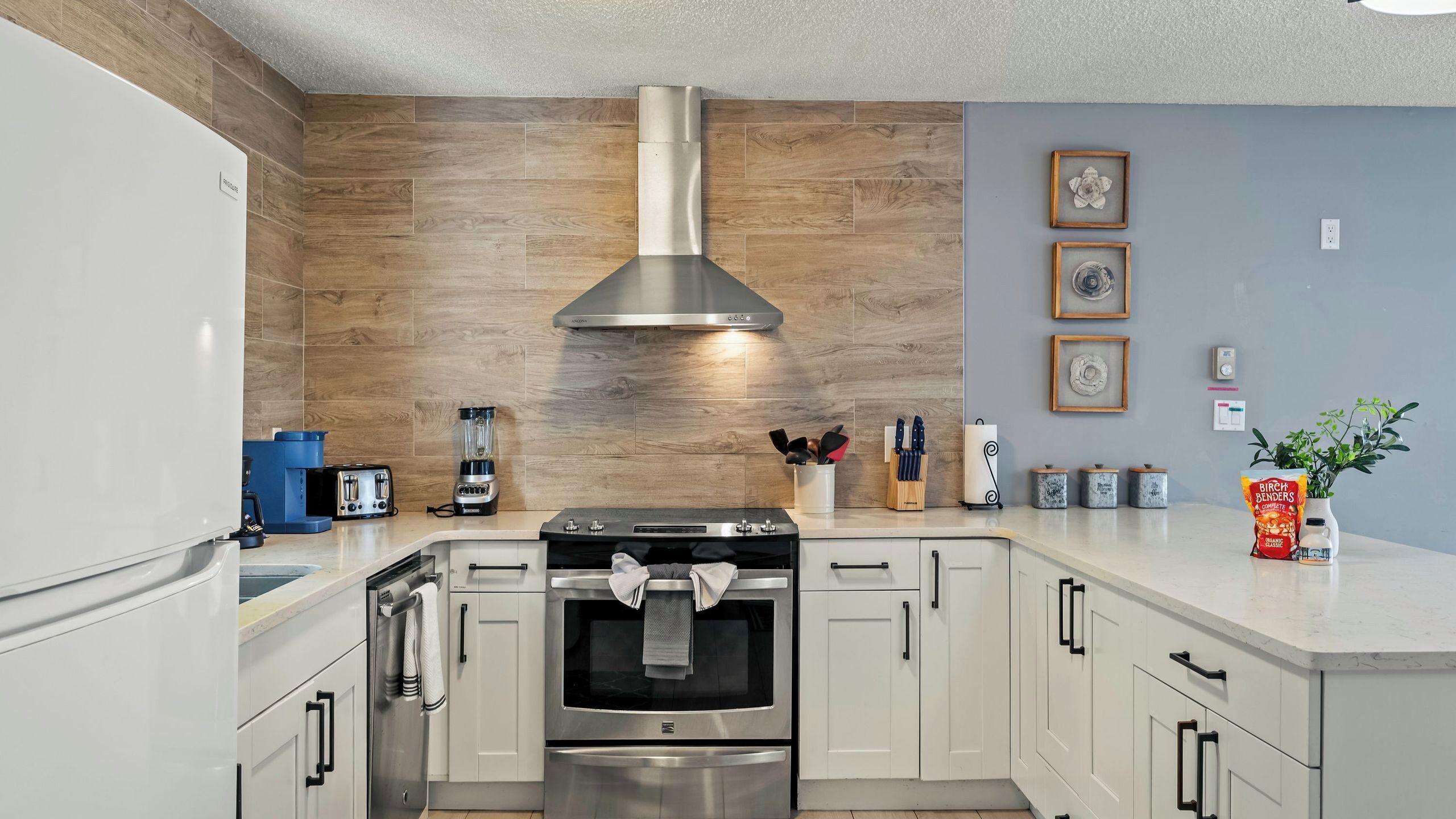 A modern kitchen with a stainless steel range hood, a built-in oven, and a dishwasher.