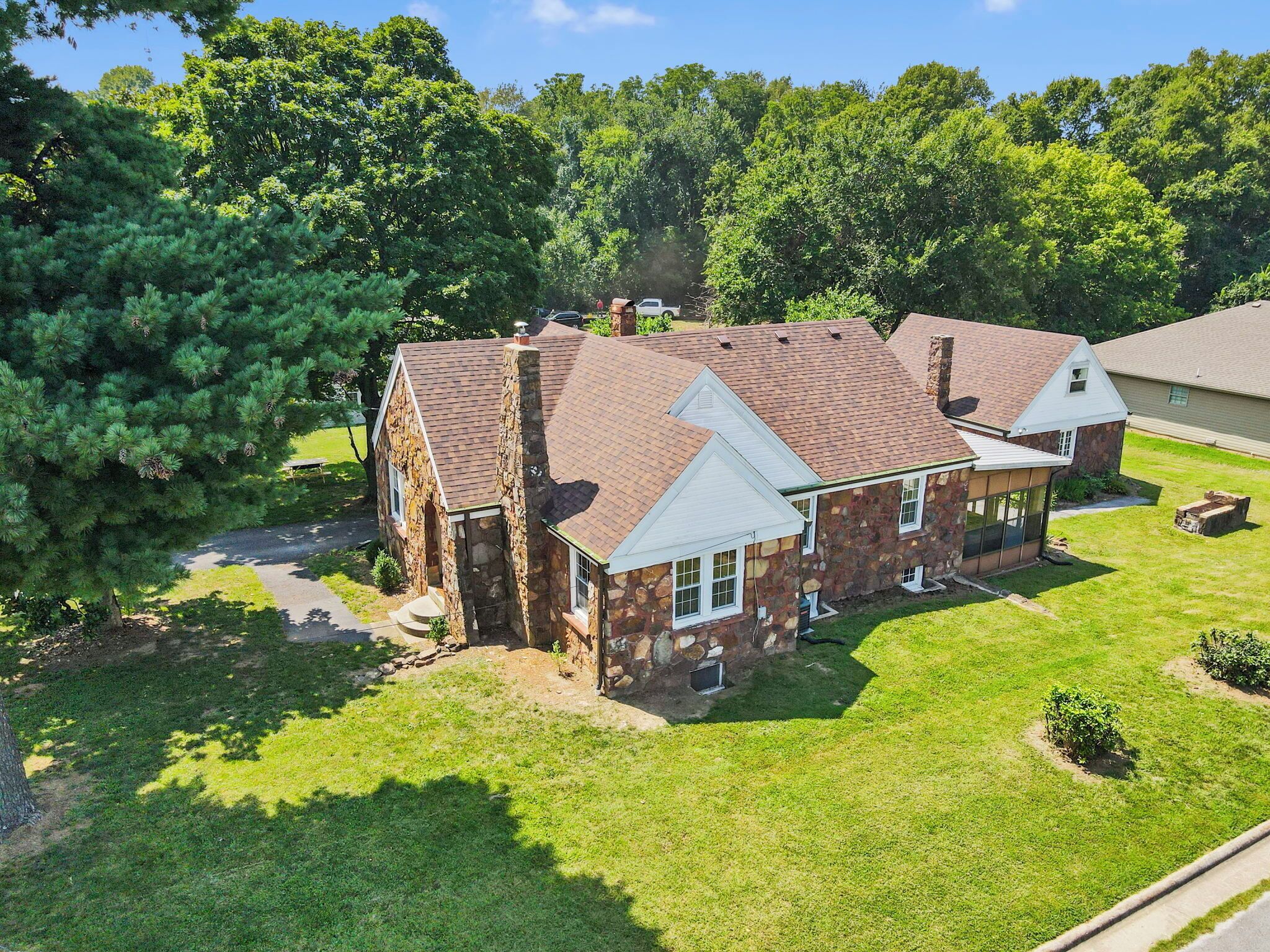 A stone house with a sloped roof, surrounded by a well-maintained lawn and trees.