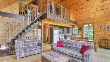 A wooden cabin interior with a staircase, two plaid sofas, a coffee table, and a kitchen area.