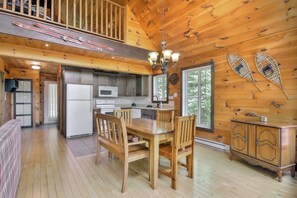 A wooden cabin interior with a dining area, kitchen, and a loft bedroom.