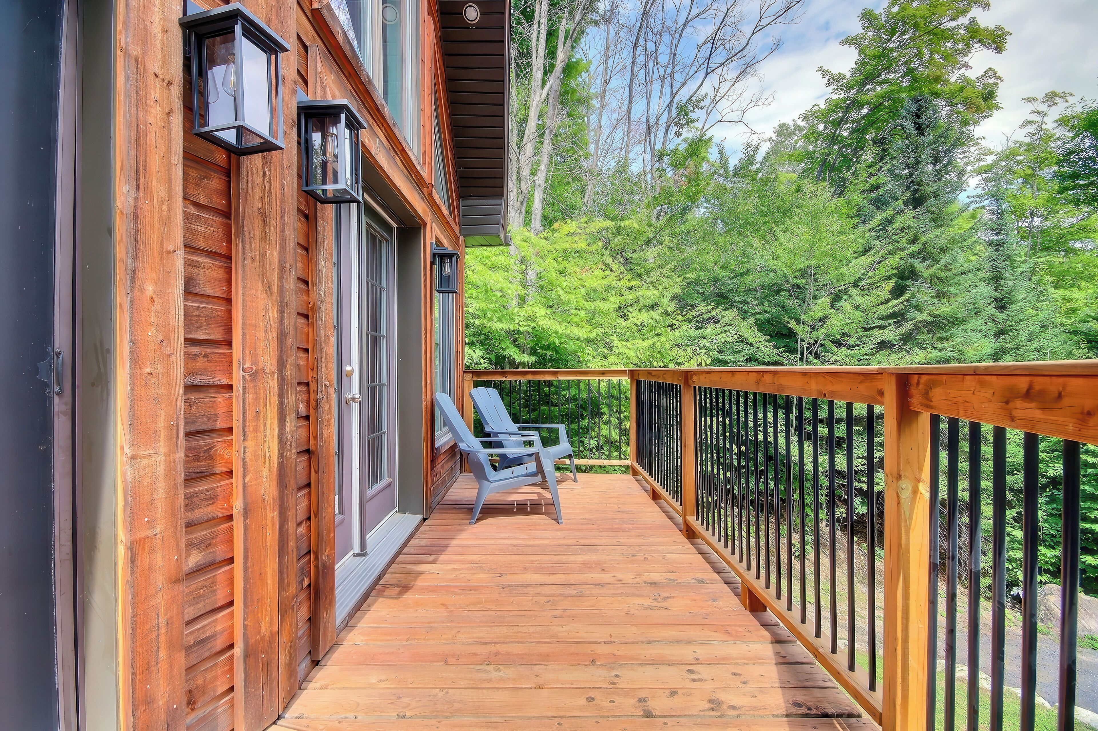 Une terrasse en bois avec une balustrade, une seule chaise bleue et une vue sur un feuillage vert et luxuriant.