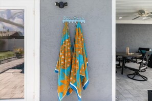 A wall-mounted towel rack with two towels hanging, a ceiling fan, and a dining area with chairs and a table. - Private Heated Pool | Lanai + Fire Pit (Largo)