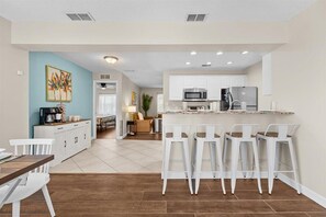 A modern kitchen with white cabinets, a central island with bar stools, and a dining area with a wooden table and white chairs.