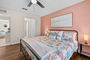 A bedroom with a bed, a ceiling fan, a nightstand, and a painting on the wall.