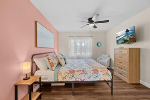 A bedroom with a bed, a nightstand, a dresser, a ceiling fan, a window with curtains, and a TV on the wall. - Private Heated Pool | Lanai + Fire Pit (Largo)