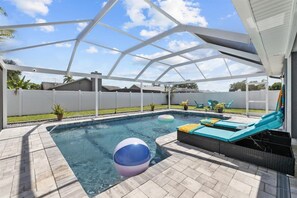 A covered outdoor swimming pool with a white roof, a lounge area with cushions, and a clear sky.