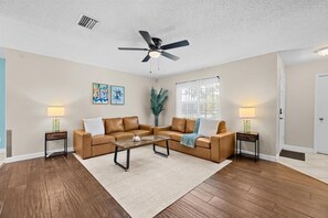 A living room with a sectional sofa, a coffee table, two side tables with lamps, a ceiling fan, and a window with curtains. - Private Heated Pool | Lanai + Fire Pit (Largo)