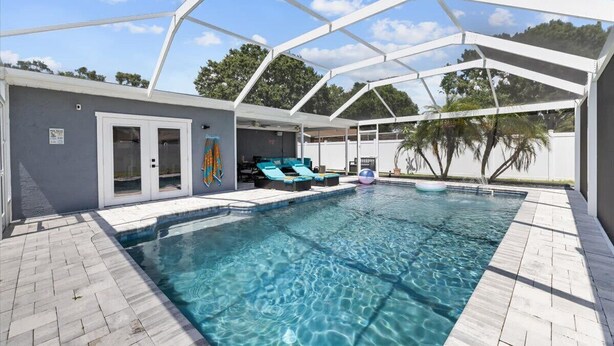A covered swimming pool with clear water, lounge chairs, and a patio area. - Private Heated Pool | Lanai + Fire Pit (Largo)