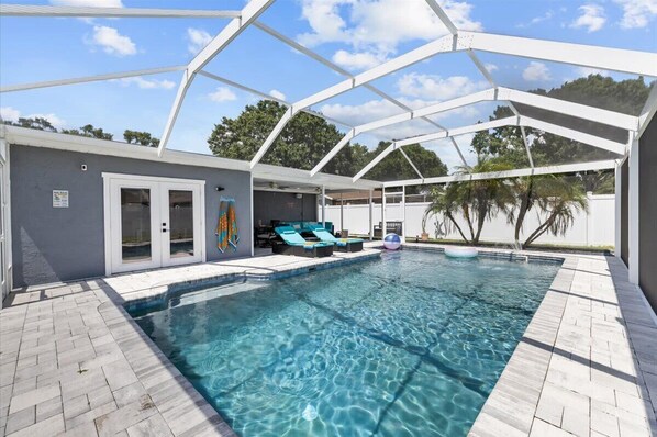 A covered swimming pool with clear water, lounge chairs, and a patio area.
