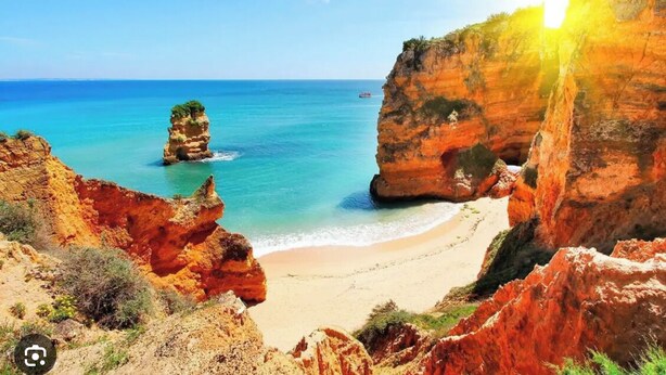 Un paysage côtier caractérisé par une formation rocheuse imposante, une plage de sable et une mer d’un bleu limpide.