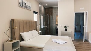 Une chambre moderne avec un grand lit, des tables de chevet, une commode, un miroir et une œuvre d’art représentant un paysage urbain accrochée au mur.
