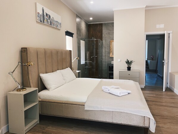 A modern bedroom with a large bed, bedside tables, a nightstand, a mirror, and a cityscape artwork on the wall.