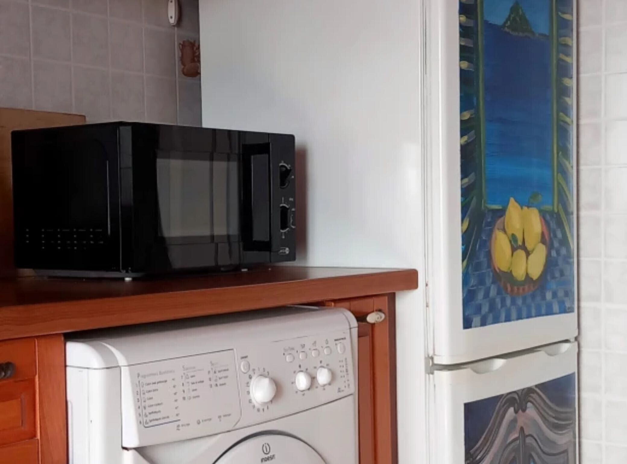 A kitchen with a microwave on a wooden countertop, a washing machine, and a refrigerator with a decorative panel.