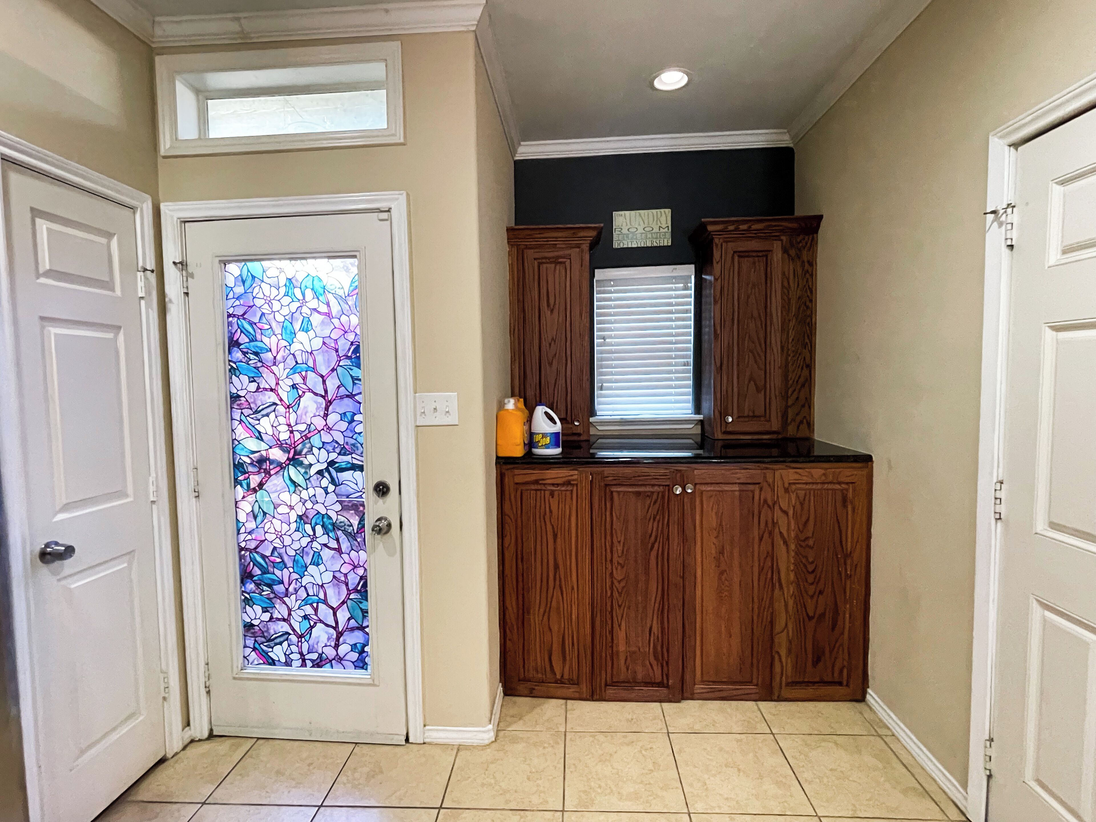 A kitchen with wooden cabinets, a stained glass door, and a window with blinds.