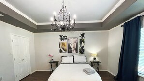 Ein Schlafzimmer mit einem großen Bett, einer Kandelaber, einem Nachttisch mit Lampe und Kunstwerken an der Wand.