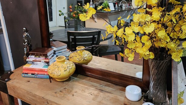 Eine hölzerne Bank mit einem Blumenstrauß aus gelben Blumen, Büchern und einem kleinen weißen Gerät.