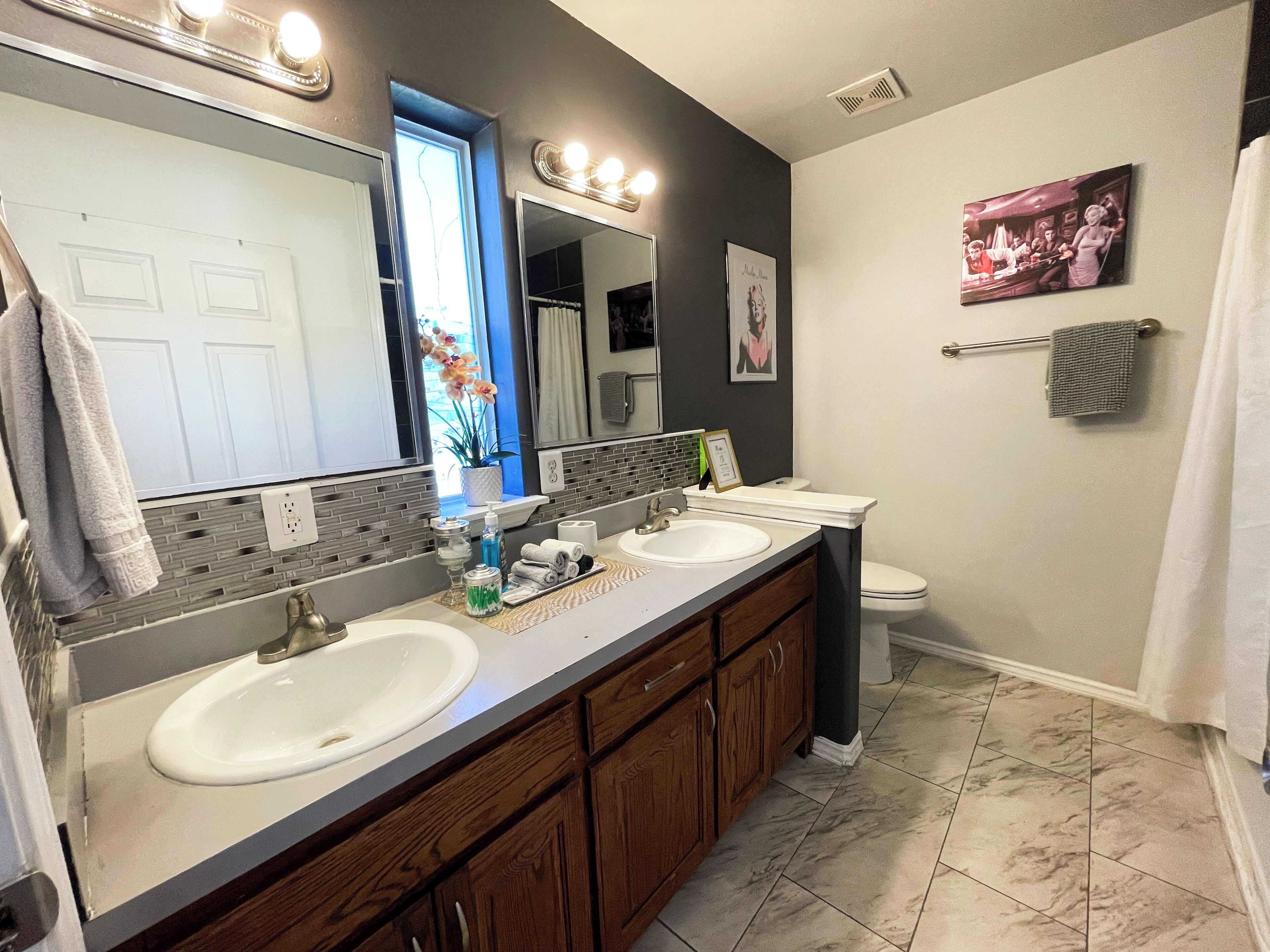 A bathroom with two sinks, a large mirror, a toilet, and a shower curtain.