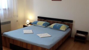 Ein Doppelbett mit Holz-Kopfteil, zwei Kissen, ein Nachttisch mit Lampe und ein kleiner Beistelltisch.