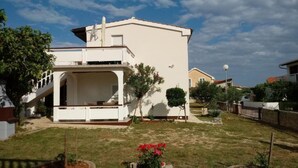 A white two-story house with a balcony and a small garden in front.