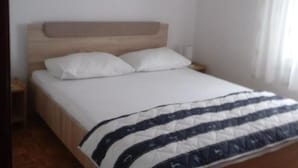 A single bed with a wooden headboard, white bedding, and a striped blanket.