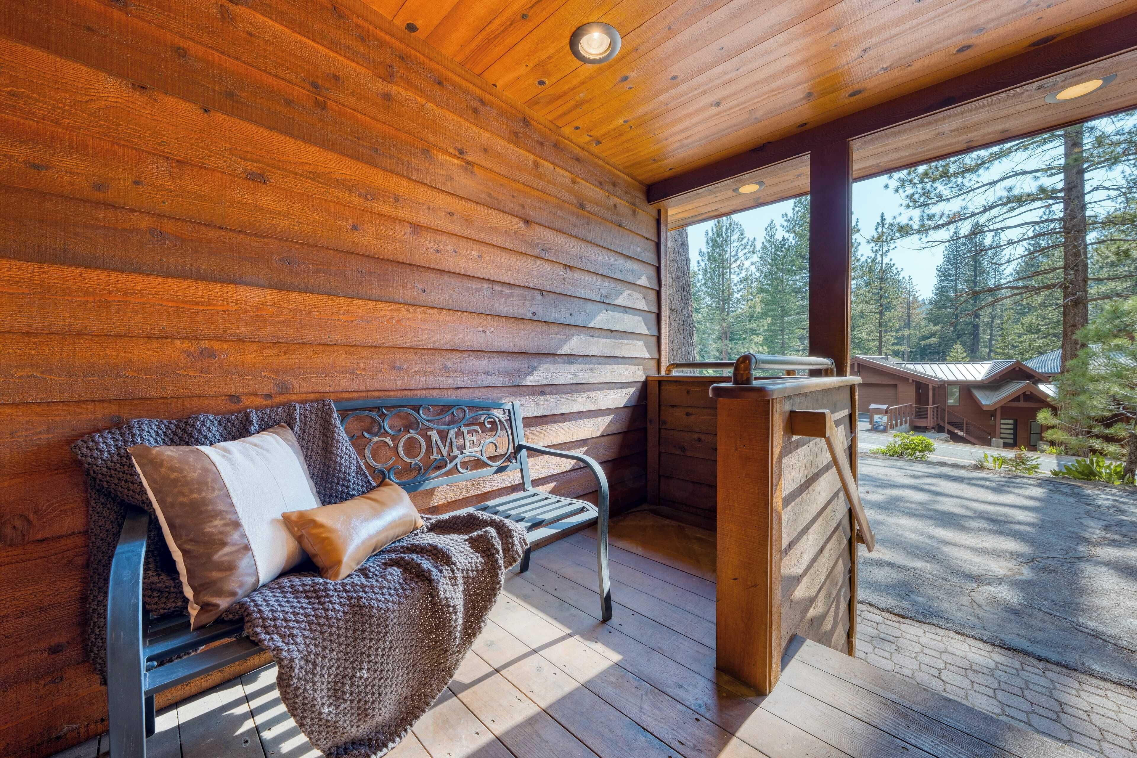 A wooden deck with a bench and a view of a forest.