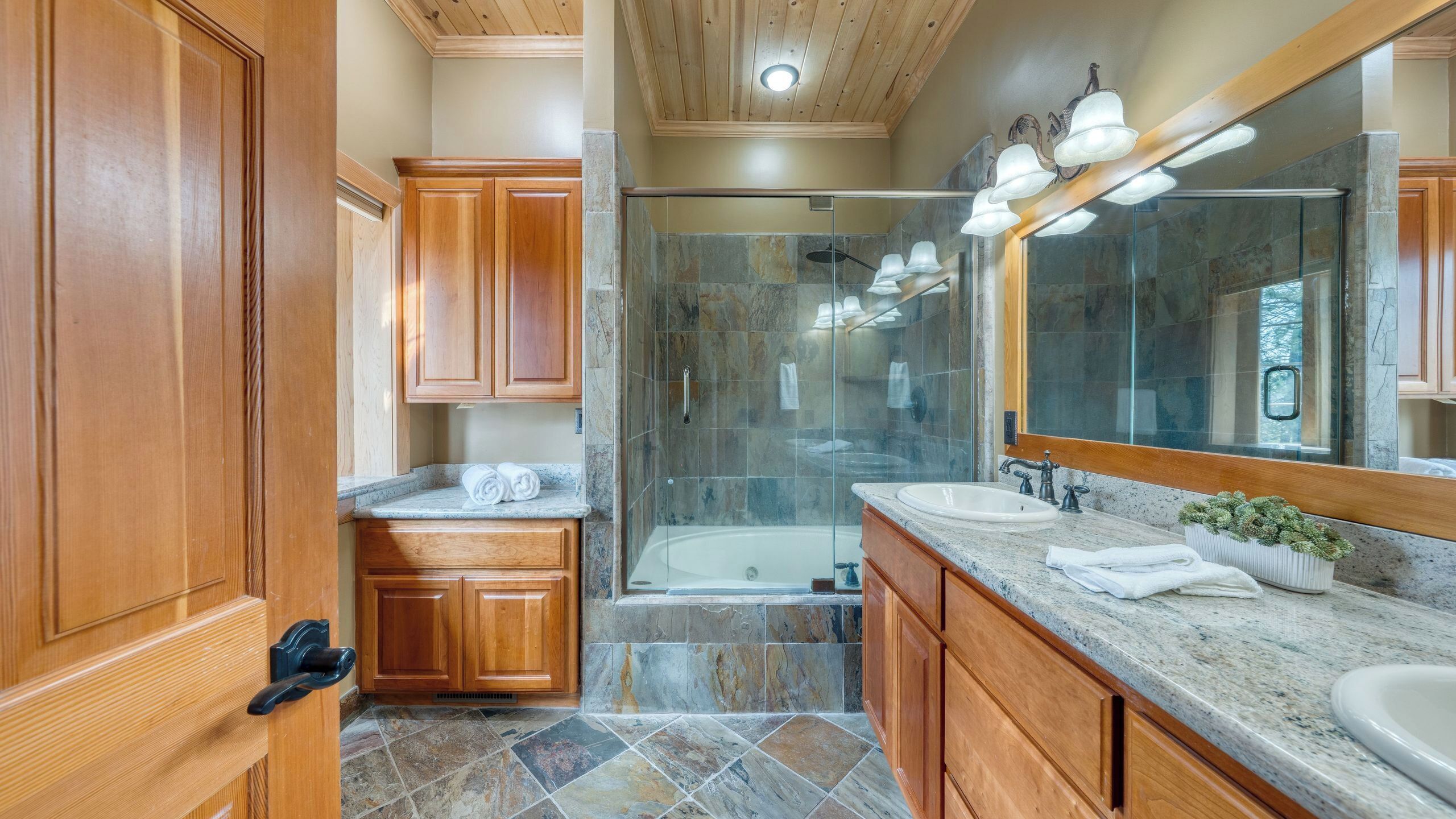 A bathroom with wooden cabinets, a glass-enclosed shower, a bathtub, and a large mirror.