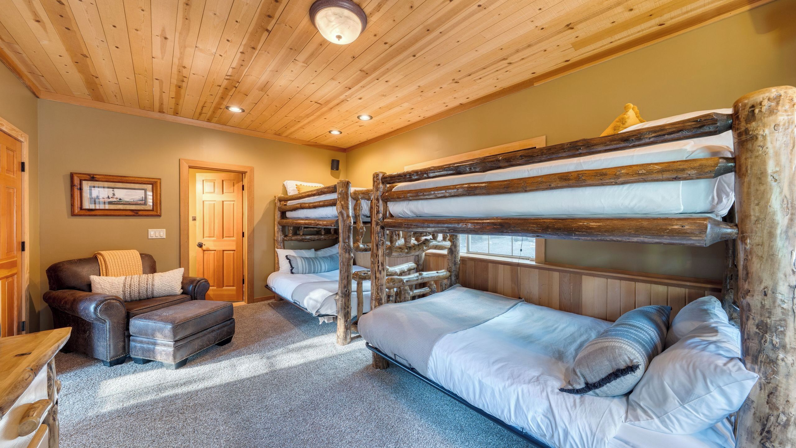 A bunk bed room with a wooden ceiling, a leather sofa, and a framed picture on the wall.