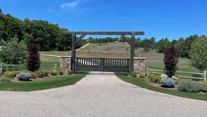 A gated entrance with a gravel driveway leading to a stone wall and a wooden pergola.