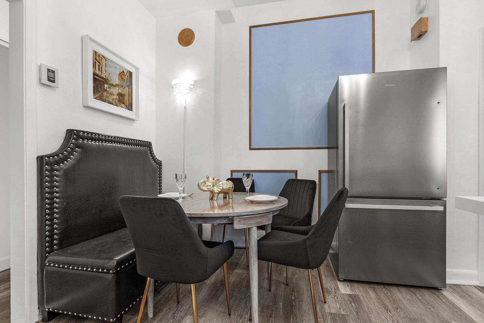 A modern dining area with a round table, black upholstered chairs, a decorative elephant figurine, and a stainless steel refrigerator.