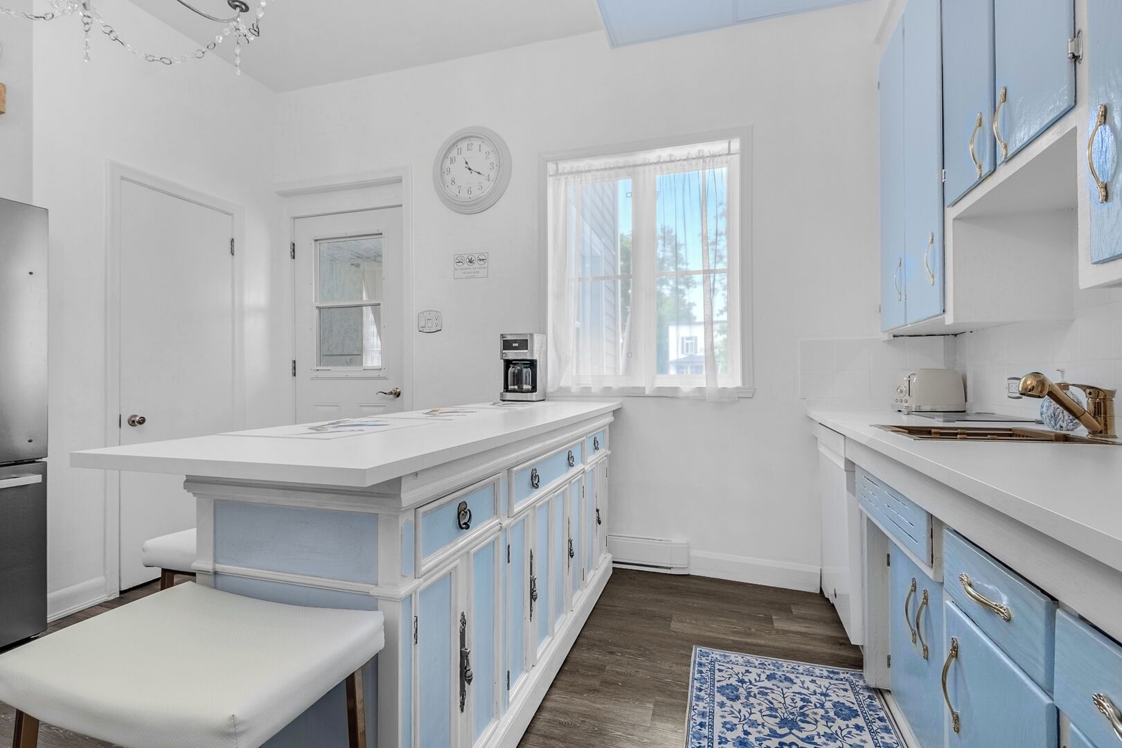 A kitchen with white and blue cabinets, a coffee maker, and a clock on the wall.