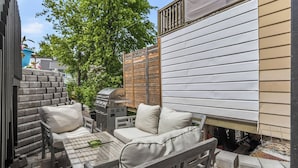 An outdoor patio with a grill, a wooden table, and a sofa.