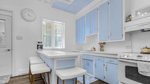 A kitchen with a central island, bar stools, a stove, and blue cabinets.