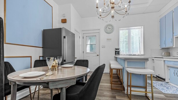 A modern kitchen with a dining area, featuring a chandelier, a clock, and light blue cabinets.