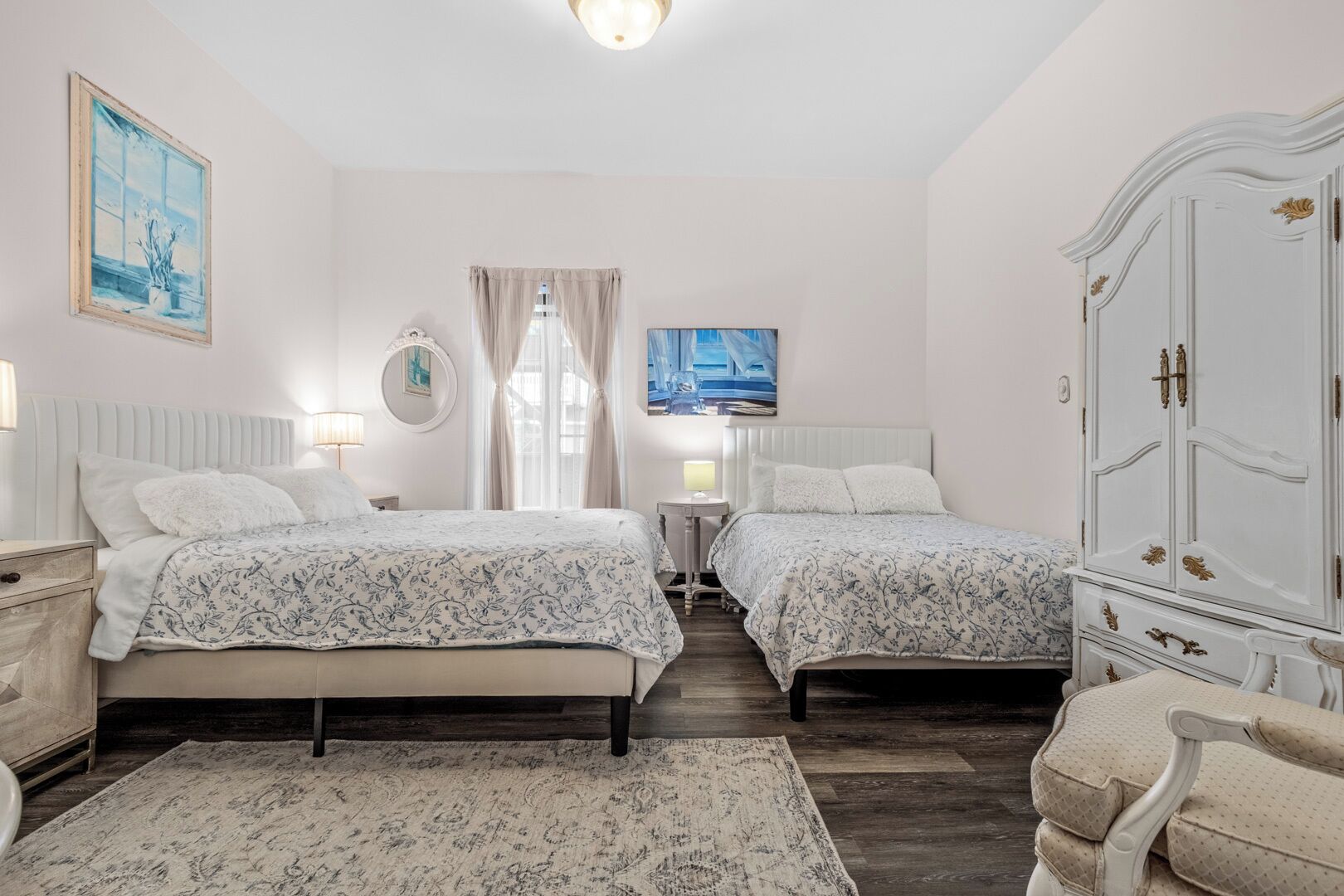 A bedroom with two beds, a wardrobe, a painting, and a window with curtains.